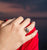 Main droite de femme déposée sur une épaule recouverte d'une vêtement rouge. La main porte à l'annulaire une bague en argent représentant un coquillage de bord de mer.